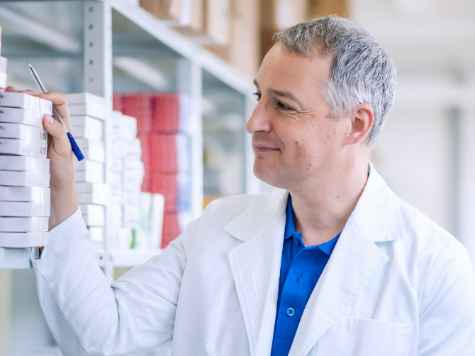 A pharmacist checking boxed stock against a list on the shelf