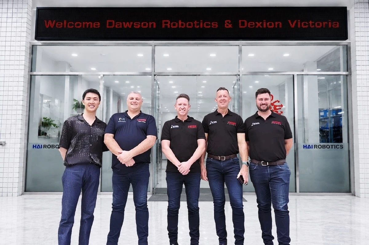 Five people standing at the entrance to Hai Robotics' facility, beneath an illuminated sign reading Welcome Dawson Robotics and Dexion Victoria