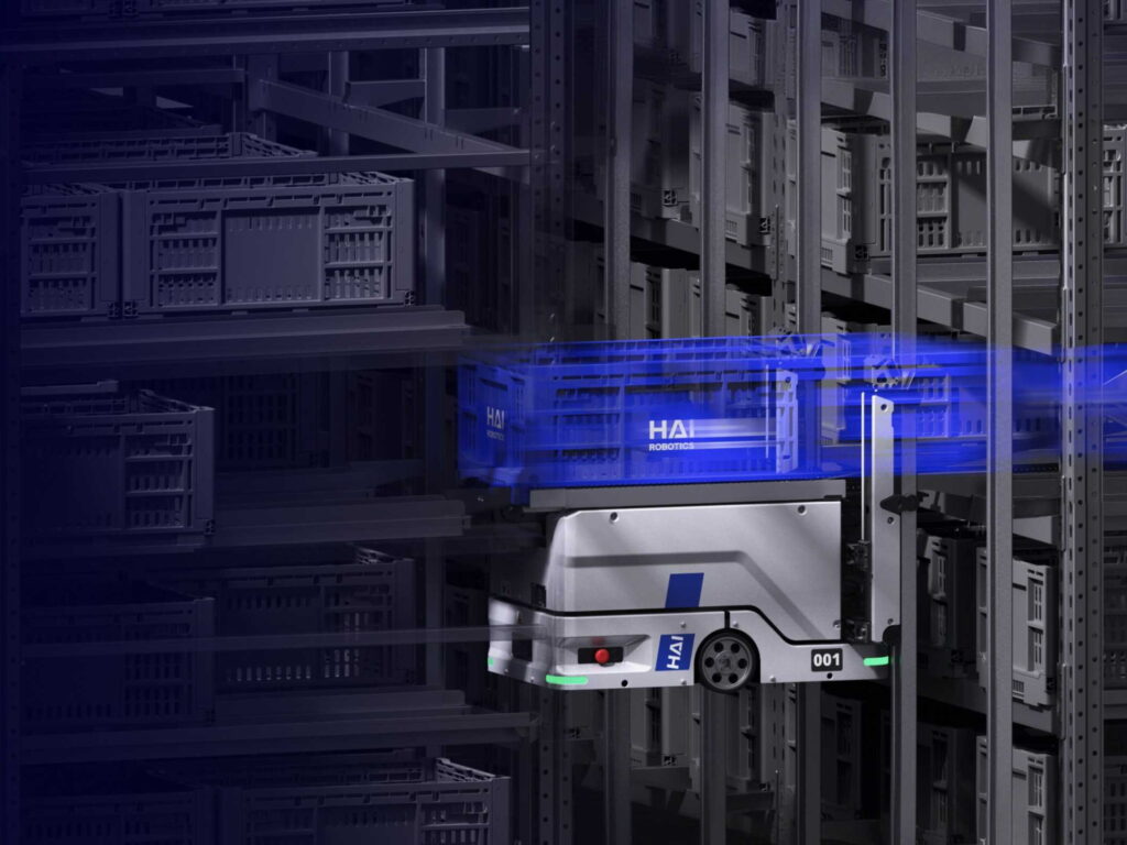 A HaiClimber robot carrying a blue tote along the face of the racking